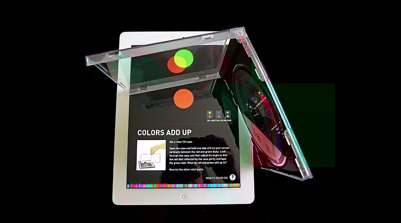 A CD jewel case held open against a Color Uncovered screen, reflecting a red disk onto a green one